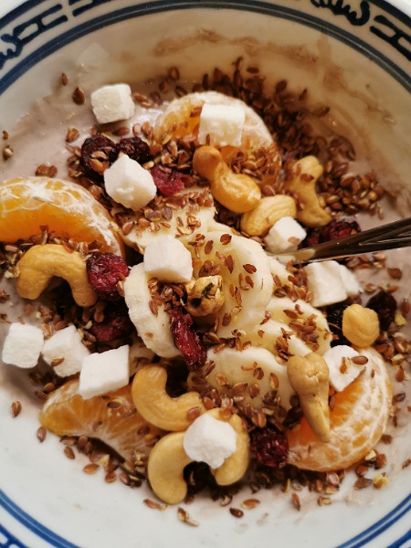 Schüssel mit Quark, Eiweißpulver, Banane, Mandarine, Goji-Beeren, Kokos und Cashewkerne