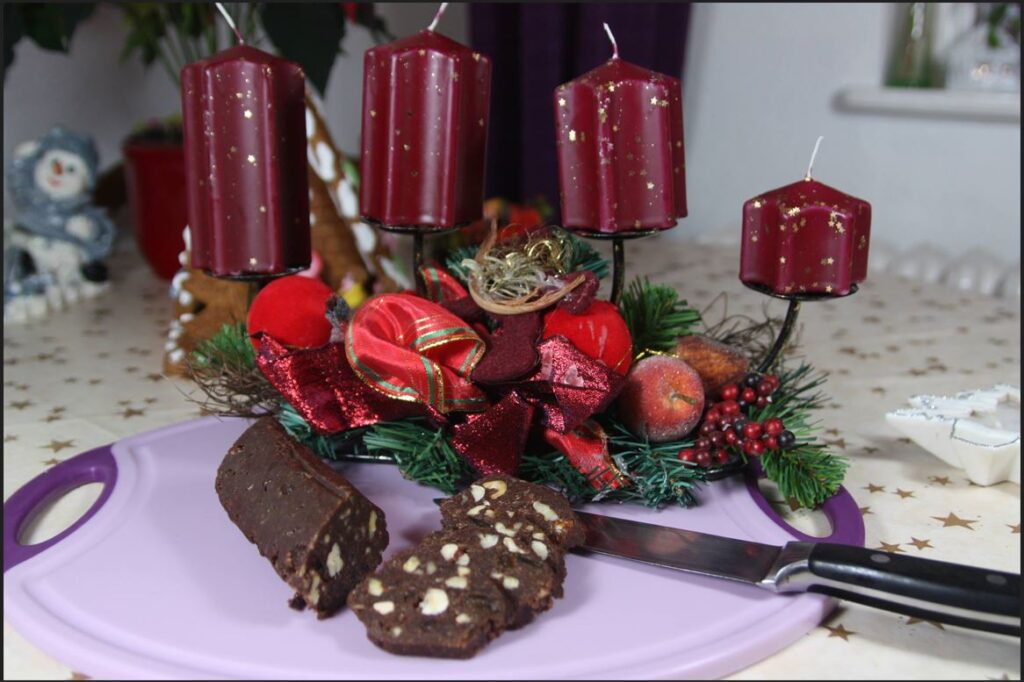 Geschnittene Schokosalami auf einem Brett vor einem weihnachtlichen Adventskranz