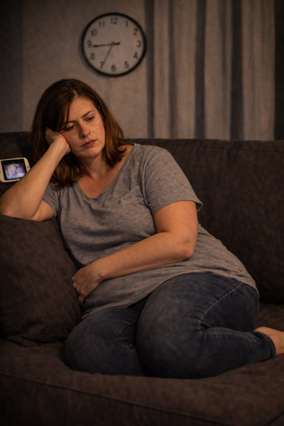 Müde und erschöpfte Frau sitzt abends allein auf dem Sofa und lehnt den Kopf auf die Hand