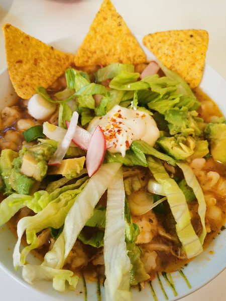 Pozole in der Schale mit frischen Beilagen, Avocado, Salat und Radieschen