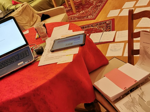 Chaotischer Schreibtisch mit Laptop, Tablet und Prüfungsunterlagen zur Vorbereitung auf die NLP-Master-Prüfung